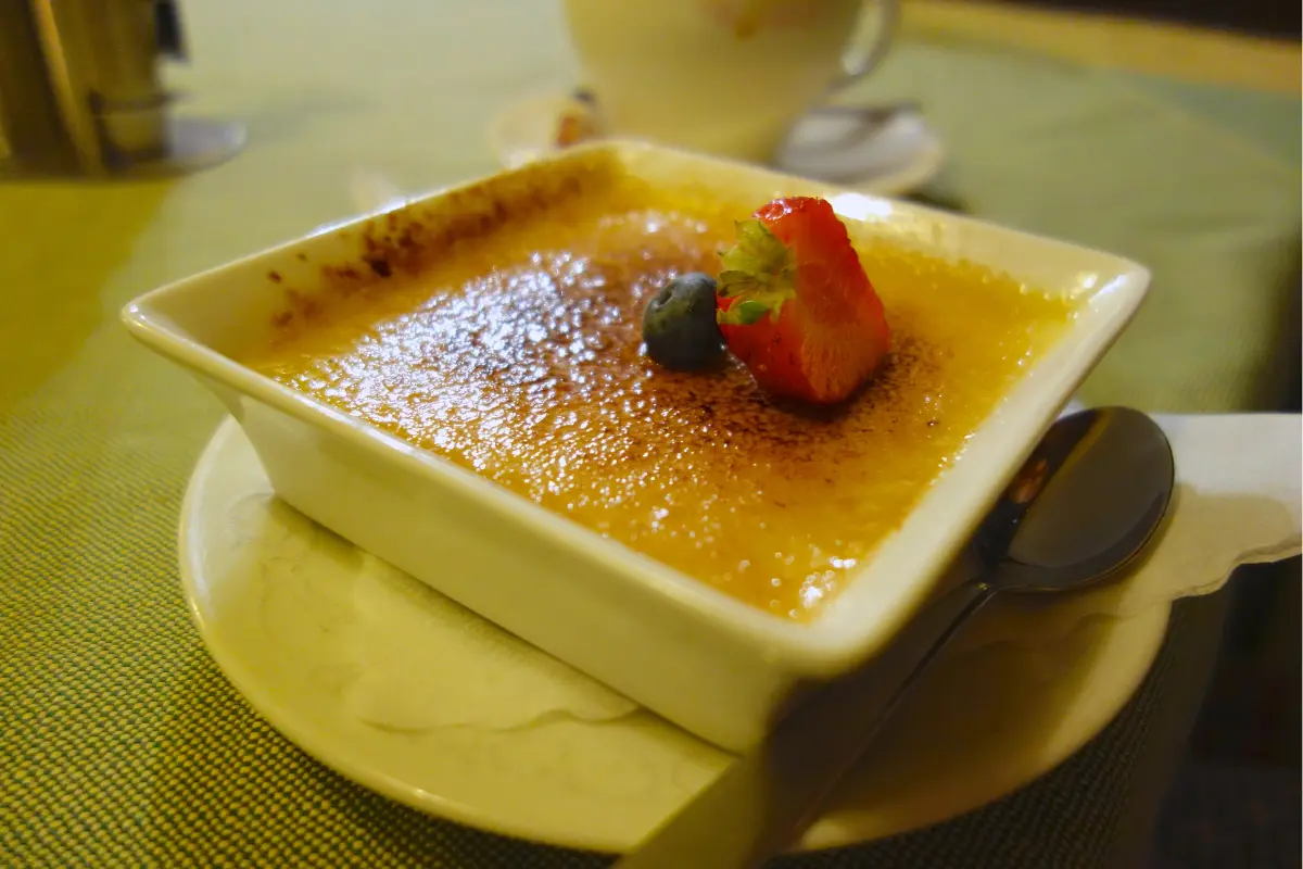 A close-up image showcasing a perfectly prepared crème brûlée with a golden caramelized top, a spoon gently breaking into the sugary crust to reveal the creamy custard beneath, set against a dark backdrop to highlight the dessert's texture and color contrast.