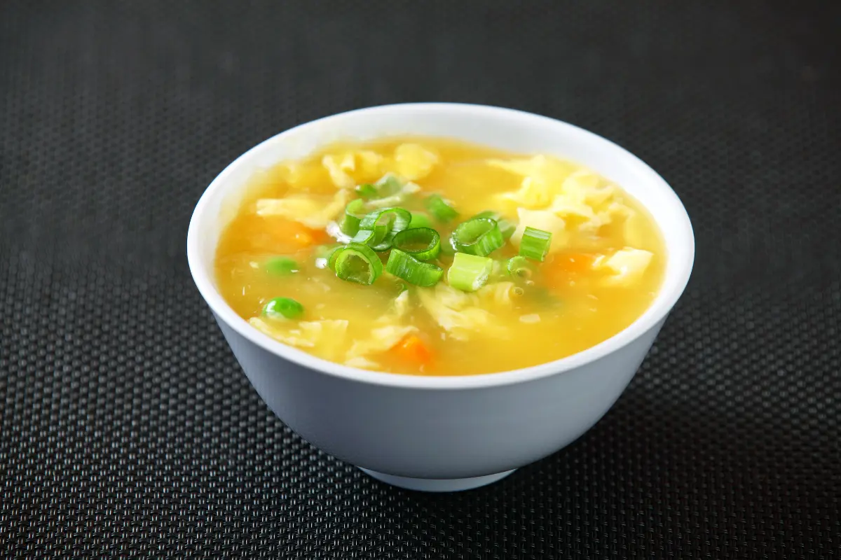 A bowl of savory wonton egg drop soup filled with silky wontons, fluffy egg ribbons, and vibrant green scallions, symbolizing a nutritious and comforting meal.