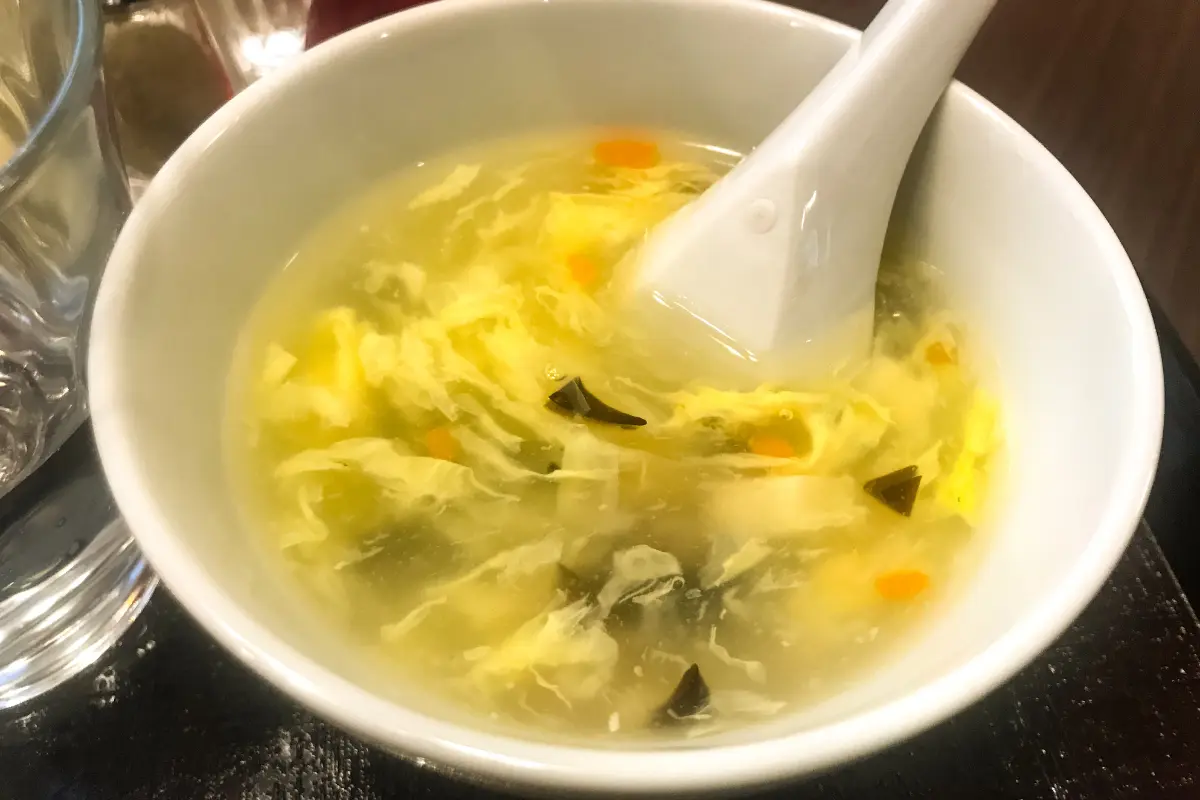 A bowl of savory wonton egg drop soup filled with silky wontons, fluffy egg ribbons, and vibrant green scallions, symbolizing a nutritious and comforting meal.