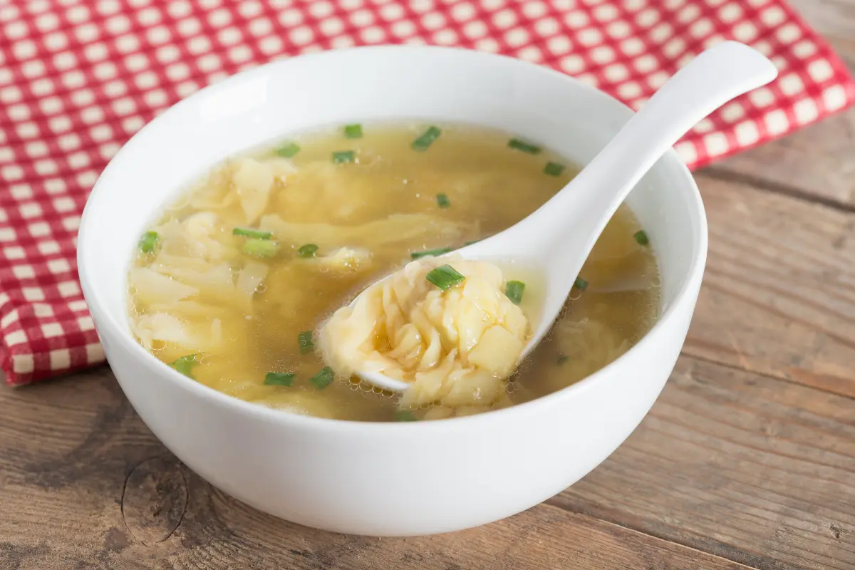 A bowl of savory wonton egg drop soup filled with silky wontons, fluffy egg ribbons, and vibrant green scallions, symbolizing a nutritious and comforting meal.