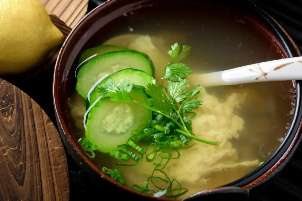 A bowl of savory wonton egg drop soup filled with silky wontons, fluffy egg ribbons, and vibrant green scallions, symbolizing a nutritious and comforting meal.