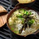 A steaming bowl of golden Chinese egg drop soup garnished with green onions and delicate egg ribbons, showcasing the simplicity and warmth of this traditional dish.