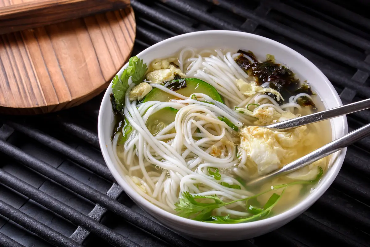 A steaming bowl of golden Chinese egg drop soup garnished with green onions and delicate egg ribbons, showcasing the simplicity and warmth of this traditional dish.