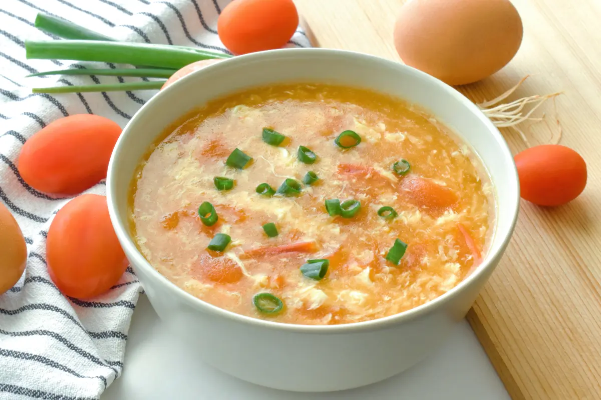 A steaming bowl of golden Chinese egg drop soup garnished with green onions and delicate egg ribbons, showcasing the simplicity and warmth of this traditional dish.