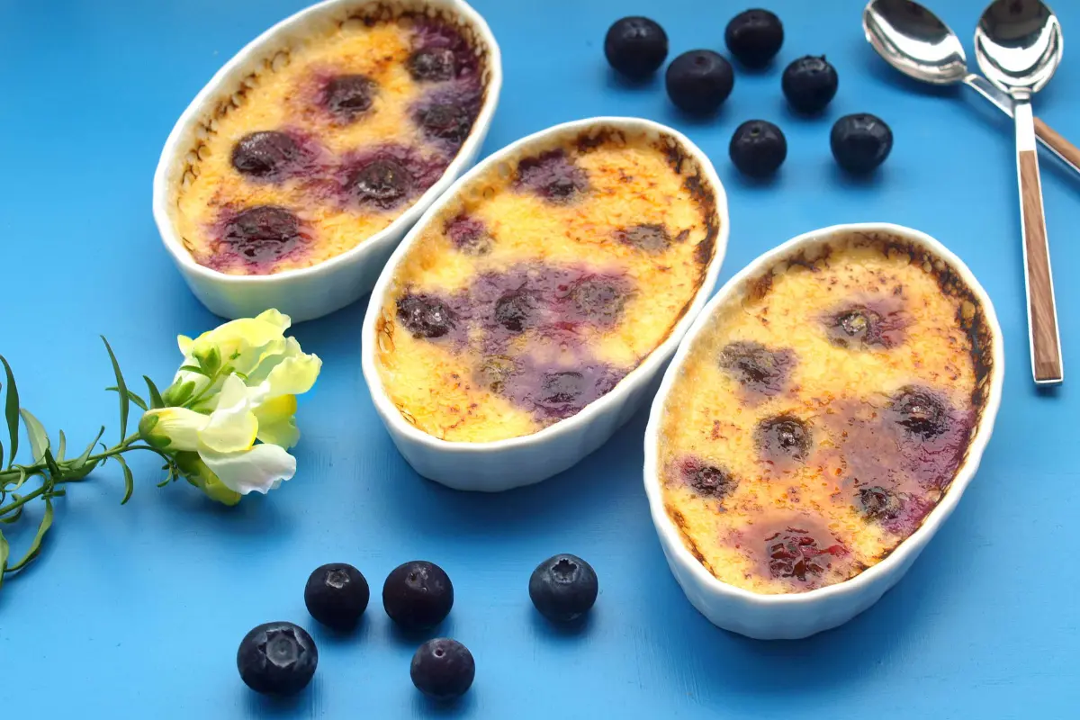 A close-up image showcasing a perfectly prepared crème brûlée with a golden caramelized top, a spoon gently breaking into the sugary crust to reveal the creamy custard beneath, set against a dark backdrop to highlight the dessert's texture and color contrast.