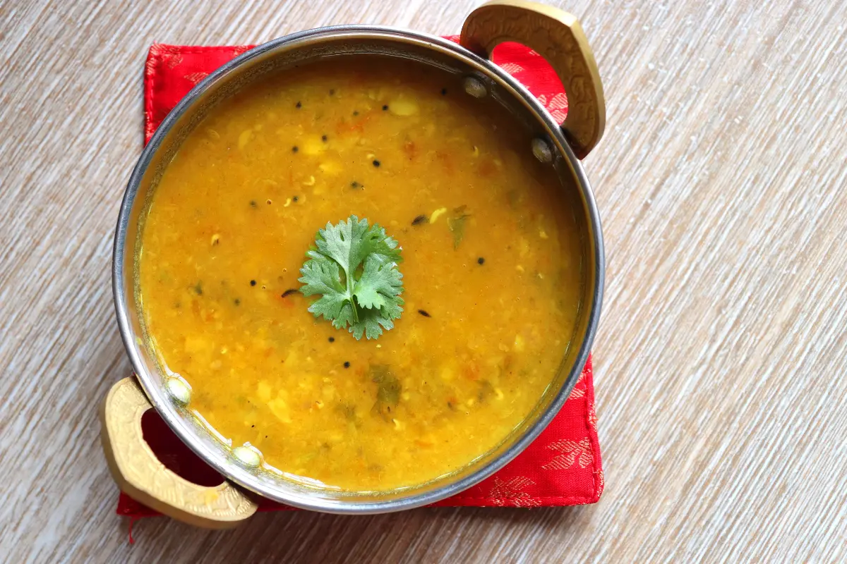 A cozy, steaming bowl of Anderson's pea soup placed on a rustic wooden table, surrounded by fresh peas, carrots, and vegan ingredients, highlighting its vegan-friendly recipe.