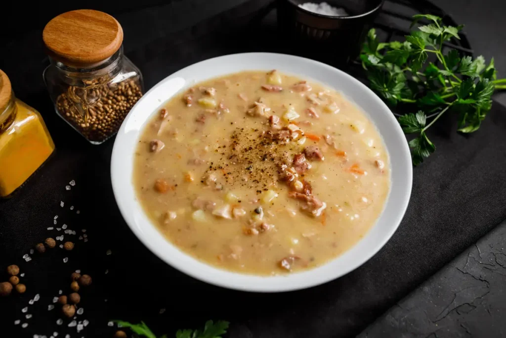 A cozy, steaming bowl of Anderson's pea soup placed on a rustic wooden table, surrounded by fresh peas, carrots, and vegan ingredients, highlighting its vegan-friendly recipe.