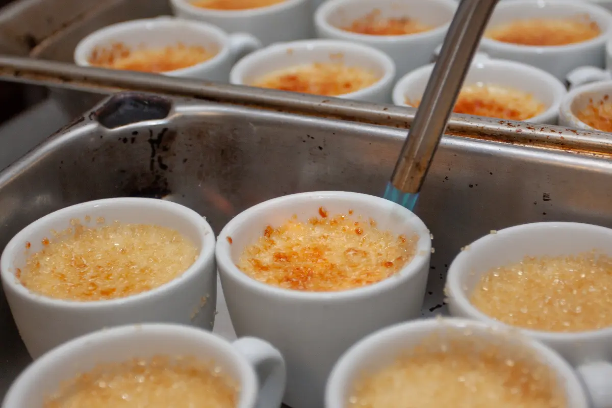 A close-up image showcasing a perfectly prepared crème brûlée with a golden caramelized top, a spoon gently breaking into the sugary crust to reveal the creamy custard beneath, set against a dark backdrop to highlight the dessert's texture and color contrast.