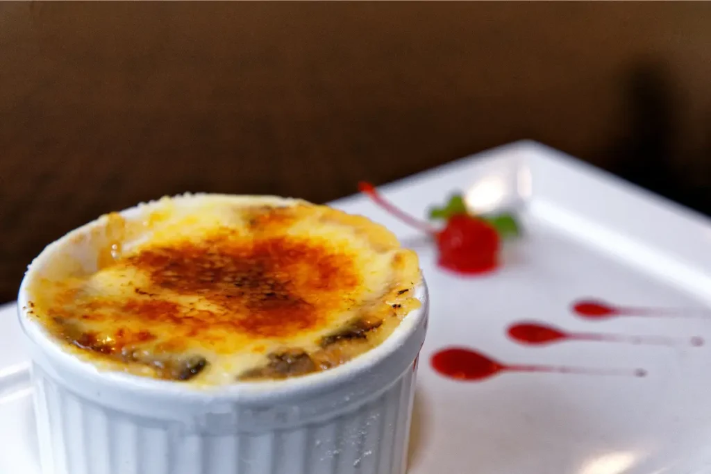 A close-up image showcasing a perfectly prepared crème brûlée with a golden caramelized top, a spoon gently breaking into the sugary crust to reveal the creamy custard beneath, set against a dark backdrop to highlight the dessert's texture and color contrast.