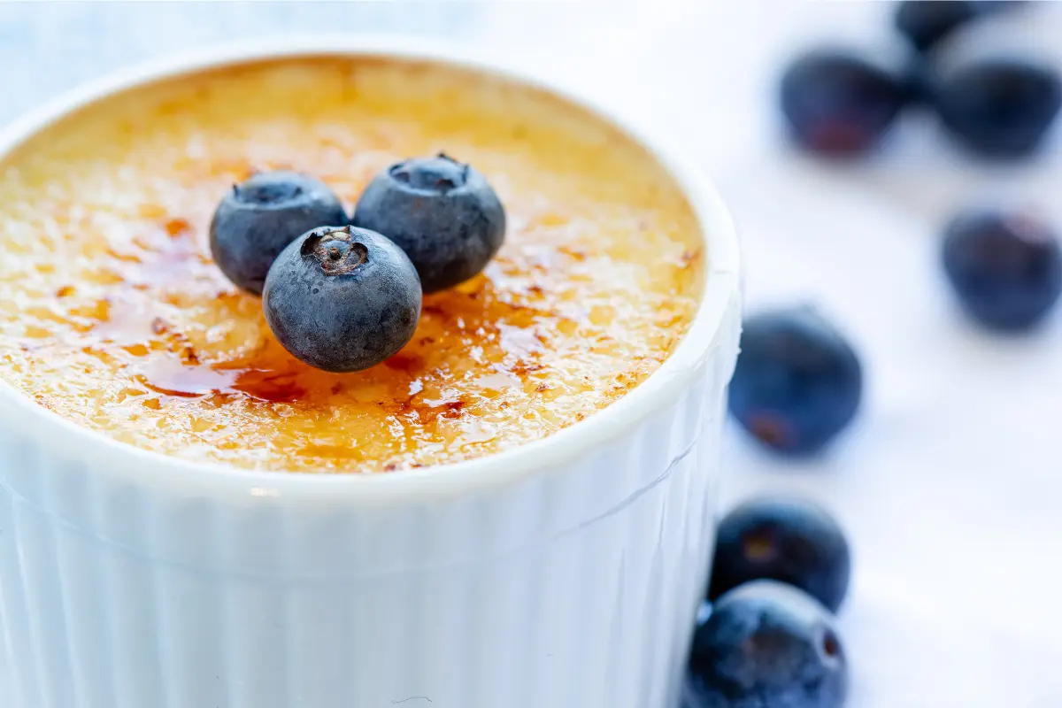 A close-up image showcasing a perfectly prepared crème brûlée with a golden caramelized top, a spoon gently breaking into the sugary crust to reveal the creamy custard beneath, set against a dark backdrop to highlight the dessert's texture and color contrast.