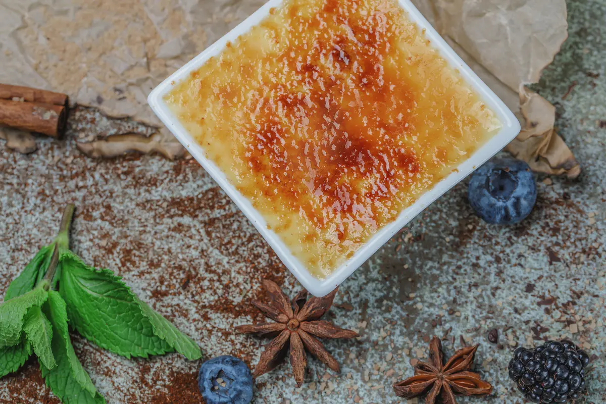 A close-up image showcasing a perfectly prepared crème brûlée with a golden caramelized top, a spoon gently breaking into the sugary crust to reveal the creamy custard beneath, set against a dark backdrop to highlight the dessert's texture and color contrast.