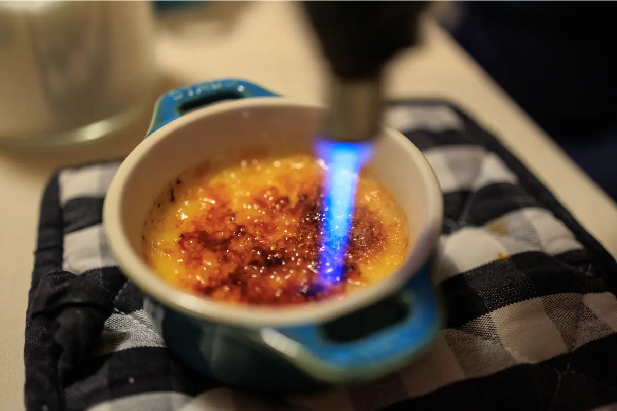 A close-up image showcasing a perfectly prepared crème brûlée with a golden caramelized top, a spoon gently breaking into the sugary crust to reveal the creamy custard beneath, set against a dark backdrop to highlight the dessert's texture and color contrast.